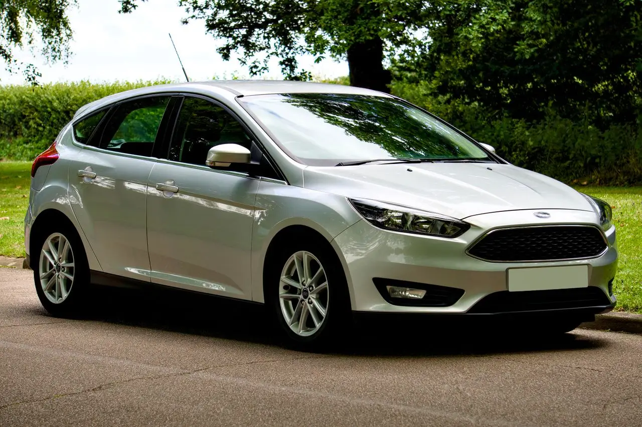 A sleek silver Ford Focus hatchback parked on a sunny day, with a scenic green background.