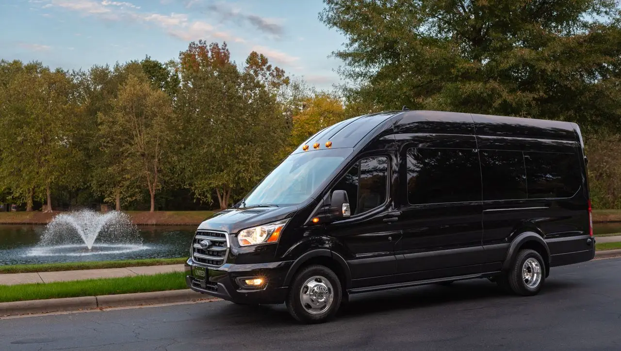 Black van parked near a serene fountain with green trees in the backdrop.